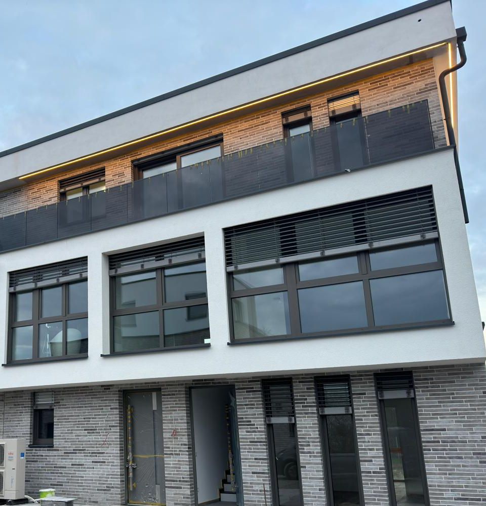 Fassade mit Klinkersockel, Glasbalustraden und warmem LED-Lichtband in der Dachkante